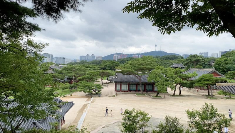 A large courtyard with a traditional Korean palace building surrounded by green trees at Changgyeonggung Palace in Seoul