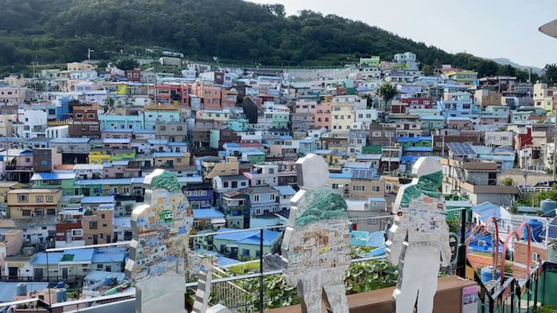 Three flat white statues of people looking out at pastel-colored village at Gamcheon Culture Village