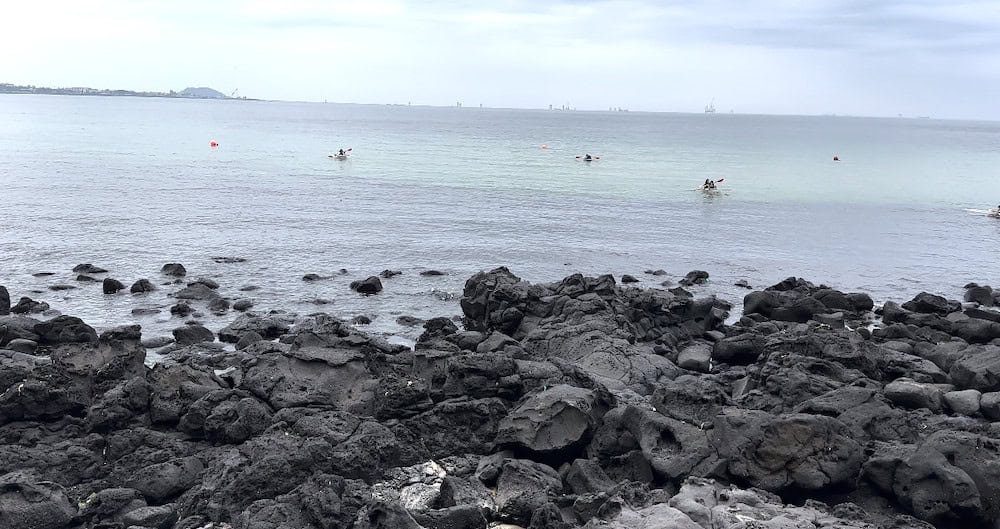 View from Aewol Cafe Street near Handam Coastal Road in Jeju with black lava rocks and teal water