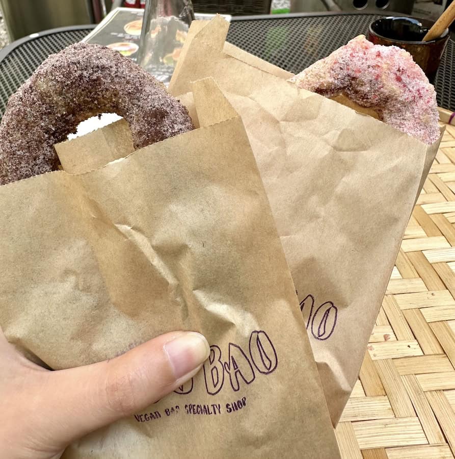 Two donuts, one chocolate and one strawberry, partially visible in brown paper bags from LUU's BAO in Osaka, Japan.