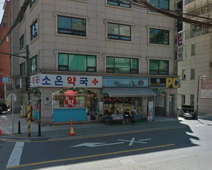 The iconic statue of King Sejong in Gwanghwamun Square, with the backdrop of the Seoul skyline and mountains, a notable scene from "XO, Kitty" Season 2.