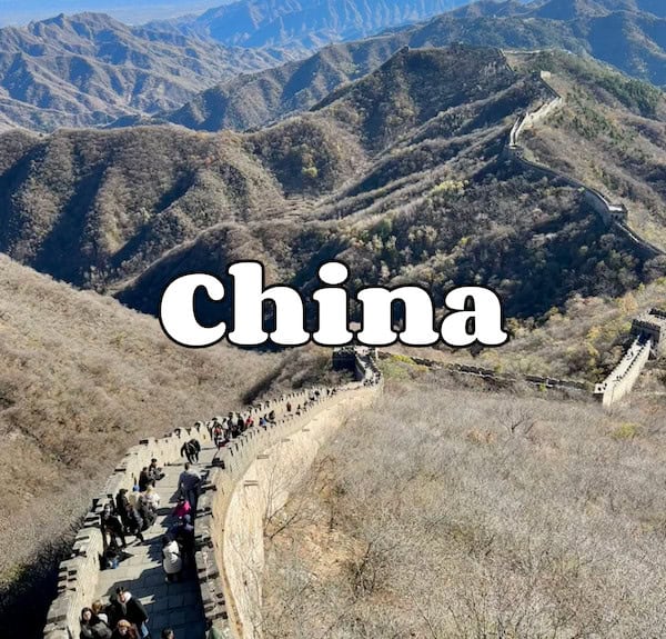 Historic Great Wall of China with tourists walking on the pathway in mountainous landscape.