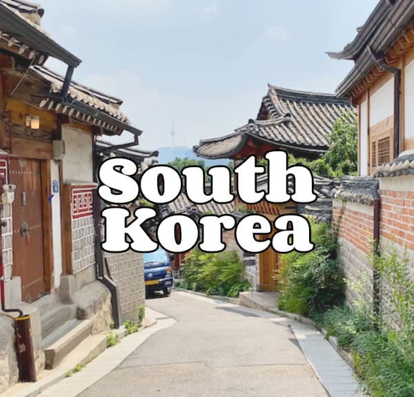Traditional Korean hanok houses in a village street. Bold white text across the center reads South Korea.